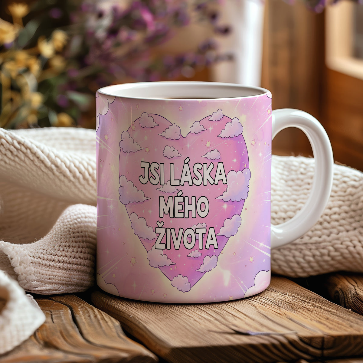 Růžový hrnek s nápisem JSI LÁSKA MÉHO ŽIVOTA obklopený mraky a hvězdami.