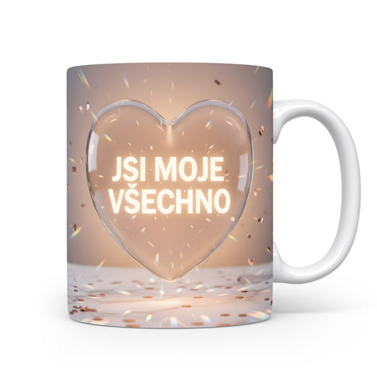 Bílý hrnek s nápisem JSI MOJE VŠECHNO v srdci na béžovém pozadí.