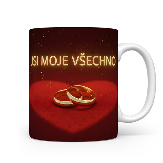 Červený hrnek s nápisem JSI MOJE VŠECHNO a zlatými prsteny na sametovém srdci.
