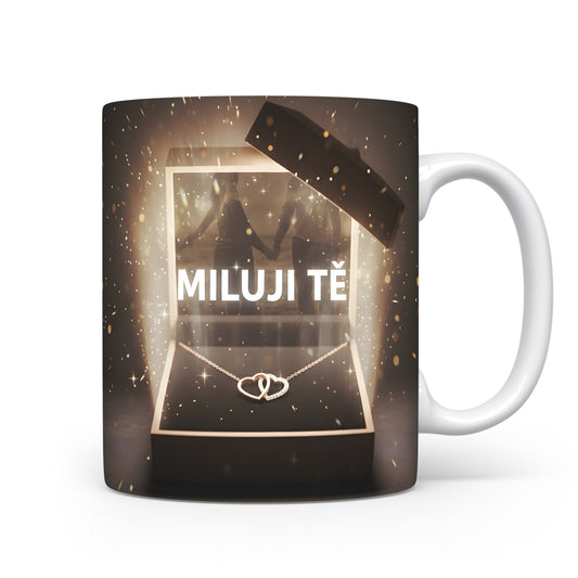 Hrnek s nápisem MILUJI TĚ a zlatými třpytkami na tmavém pozadí.