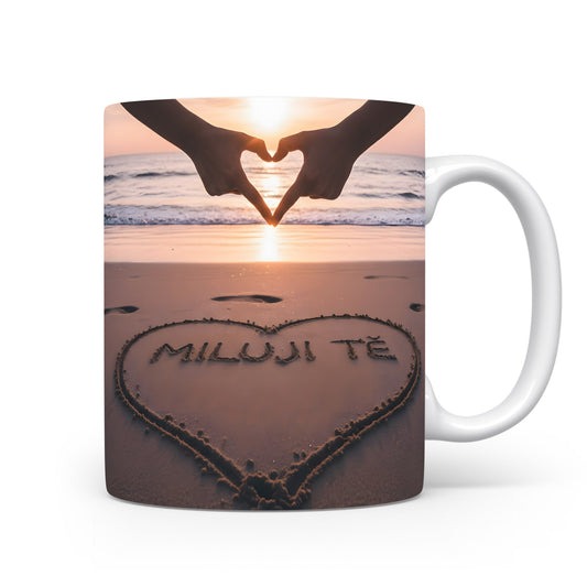 Hrnček s nápisem MILUJI TĚ na pláži při západu slunce.