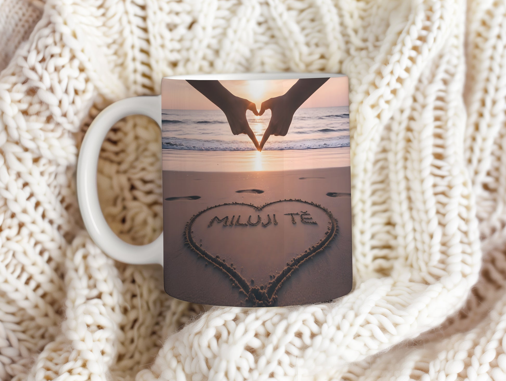 Hrnček s nápisem MILUJI TĚ na pláži při západu slunce.