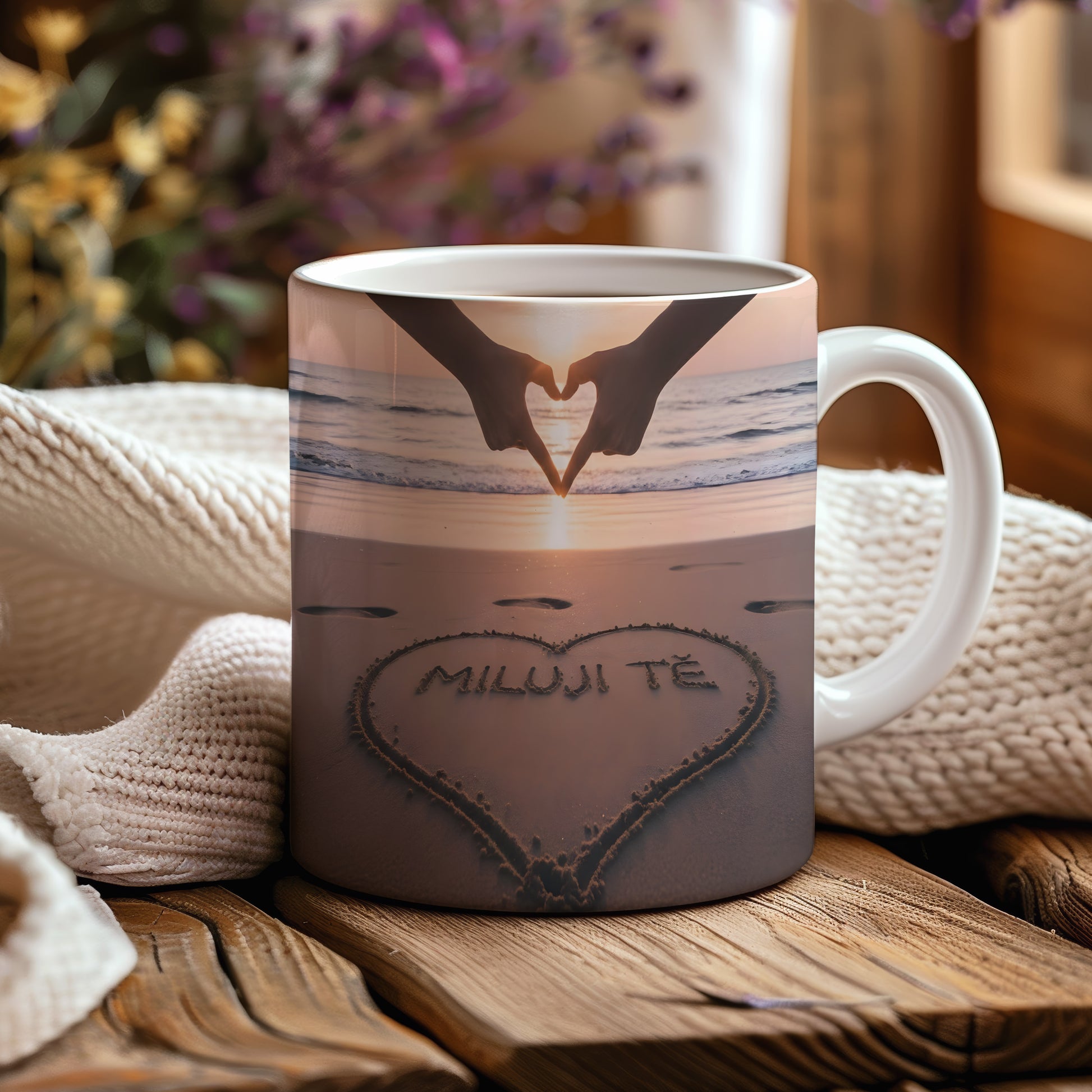 Hrnček s nápisem MILUJI TĚ na pláži při západu slunce.