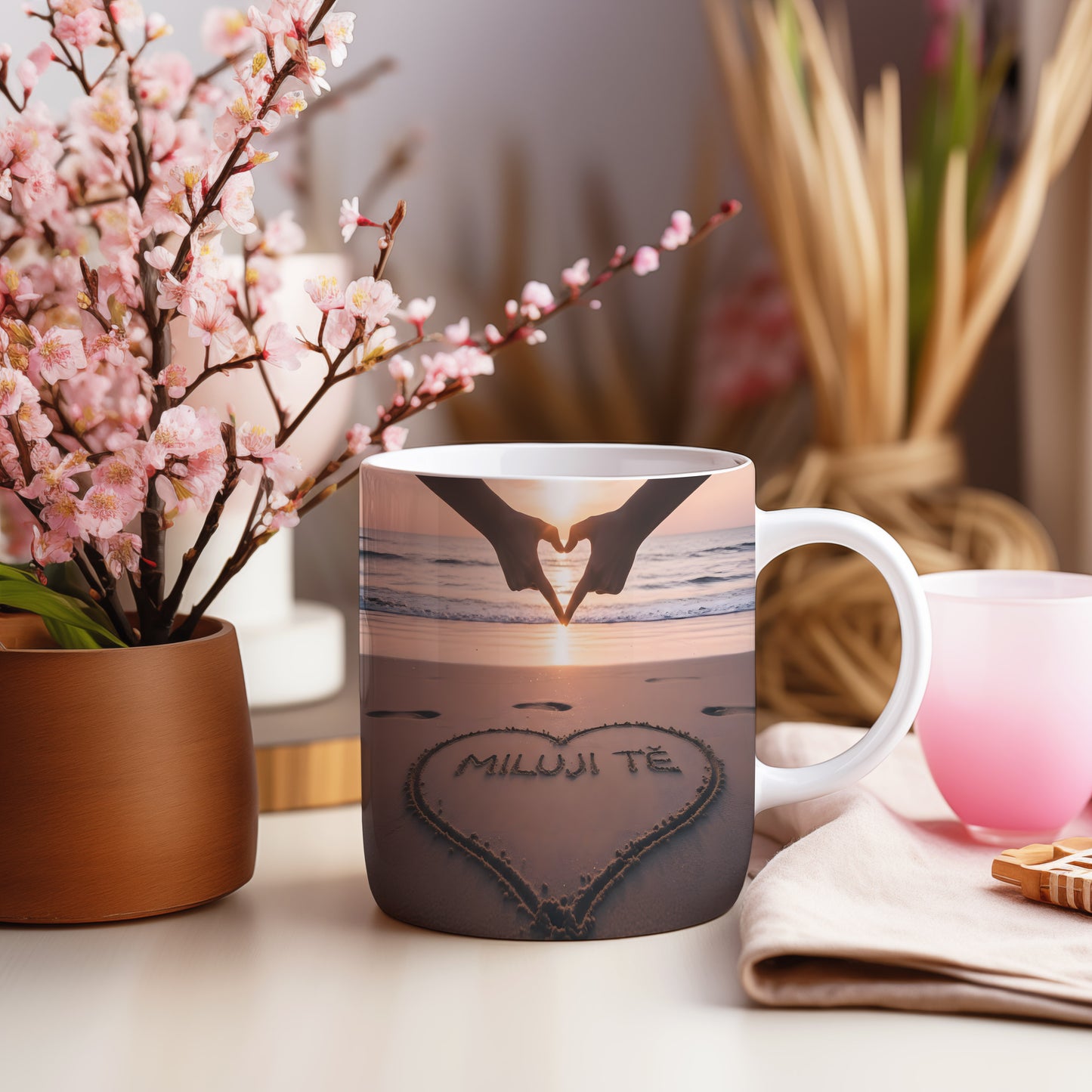 Hrnček s nápisem MILUJI TĚ na pláži při západu slunce.