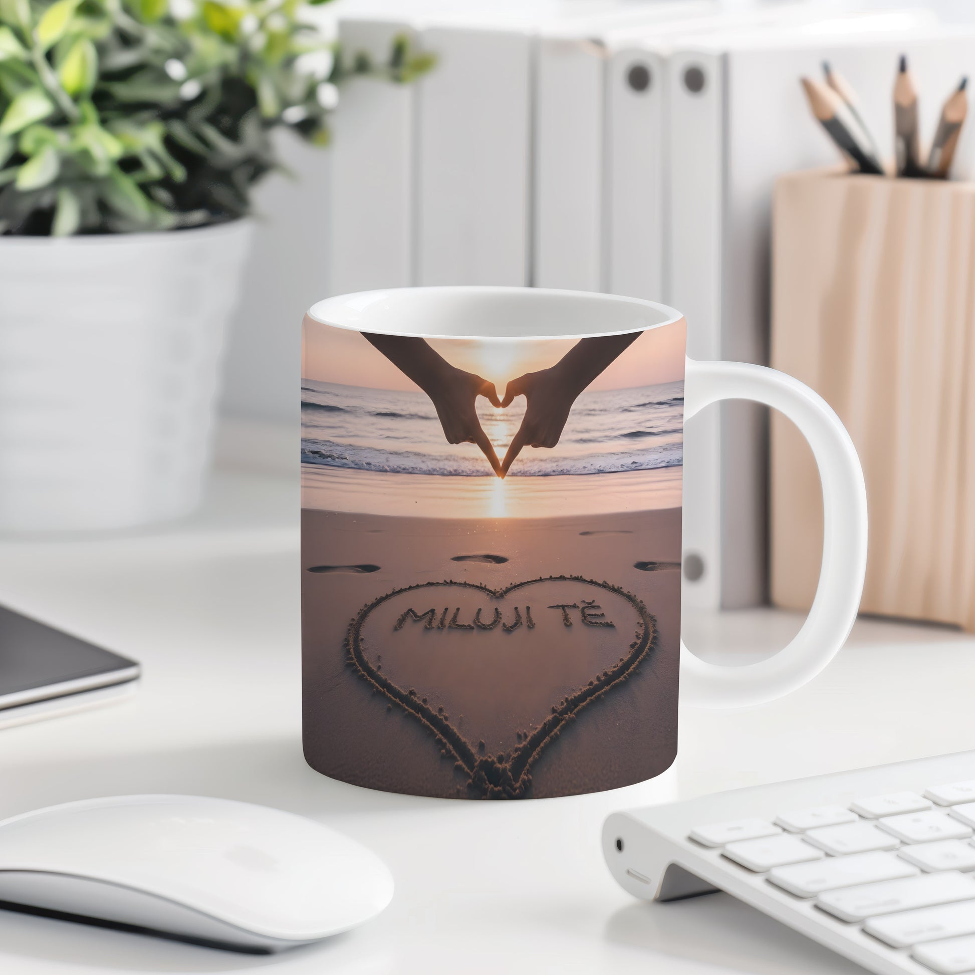 Hrnček s nápisem MILUJI TĚ na pláži při západu slunce.