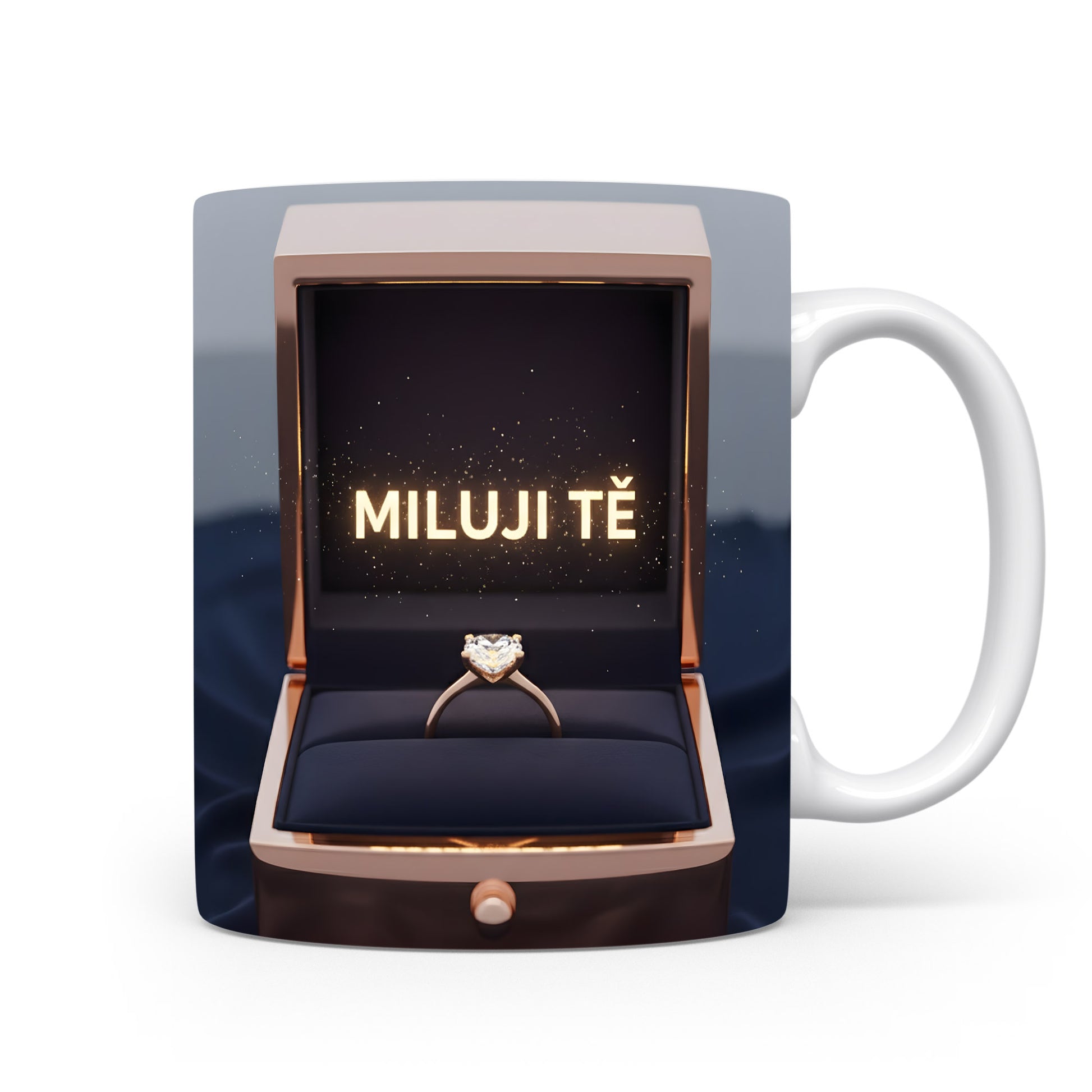 Hrnček s nápisem MILUJI TĚ a zlatým prstenem v krabičce.