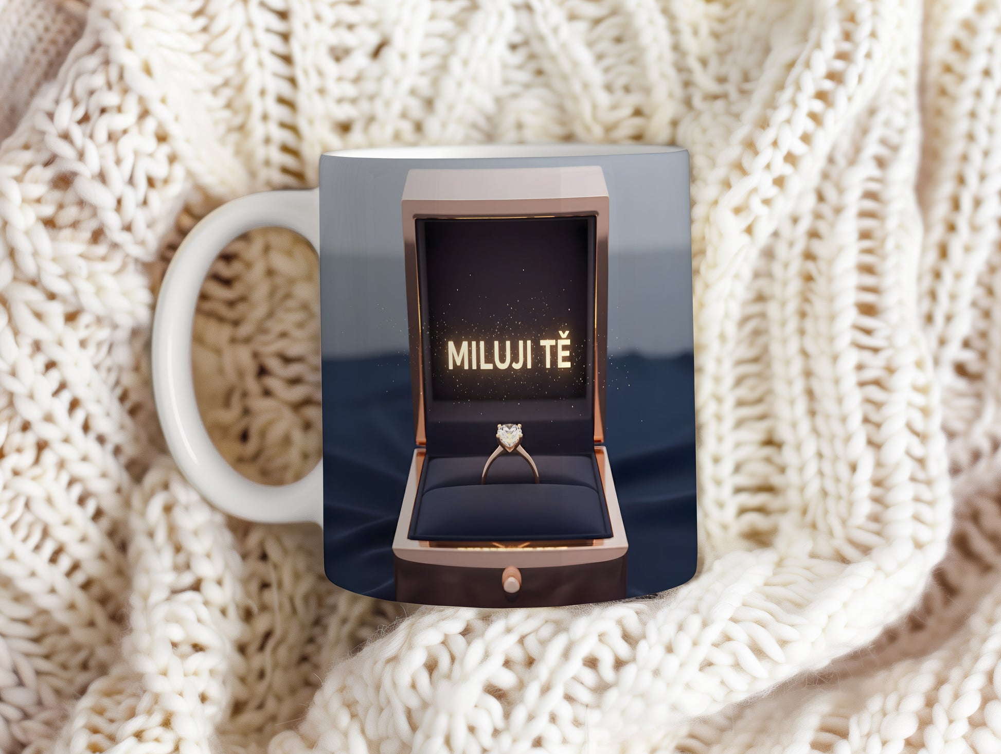 Hrnček s nápisem MILUJI TĚ a zlatým prstenem v krabičce.