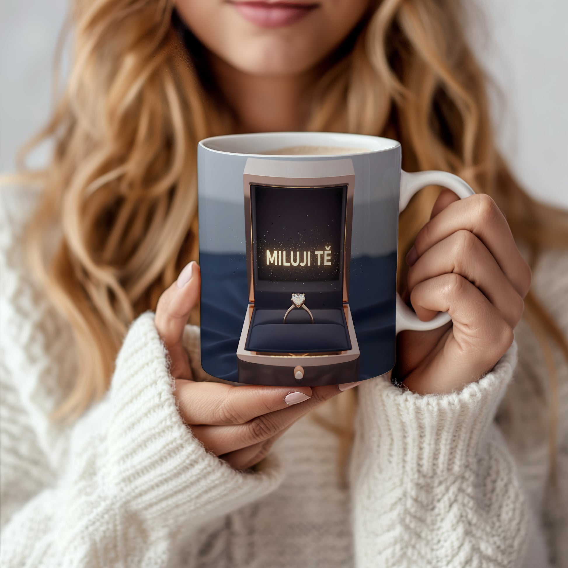 Hrnček s nápisem MILUJI TĚ a zlatým prstenem v krabičce.