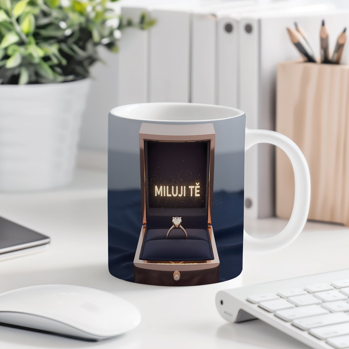 Hrnček s nápisem MILUJI TĚ a zlatým prstenem v krabičce.