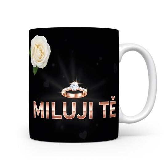 Černý hrnek s nápisem MILUJI TĚ, prstenem a bílou růží.