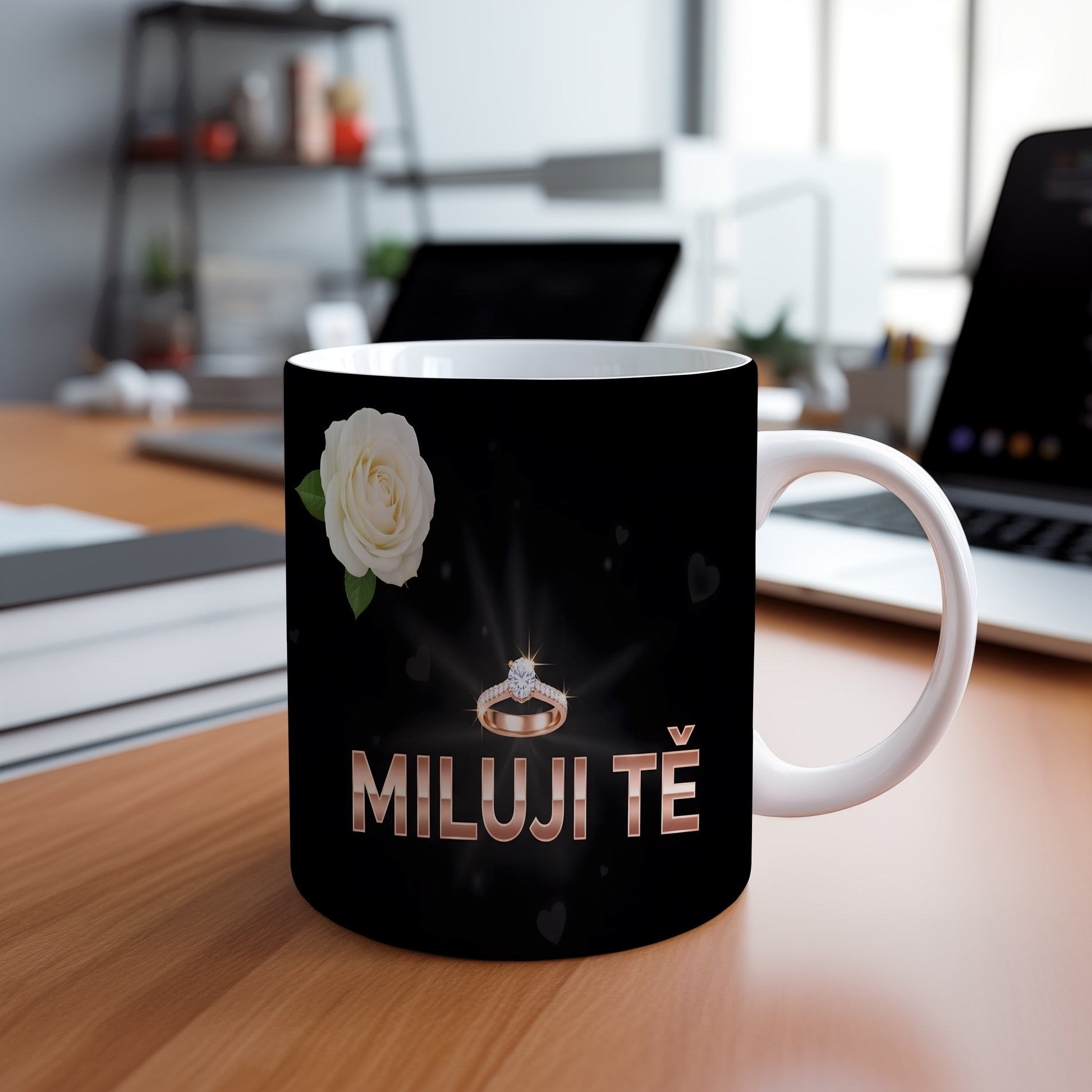 Černý hrnek s nápisem MILUJI TĚ, prstenem a bílou růží.