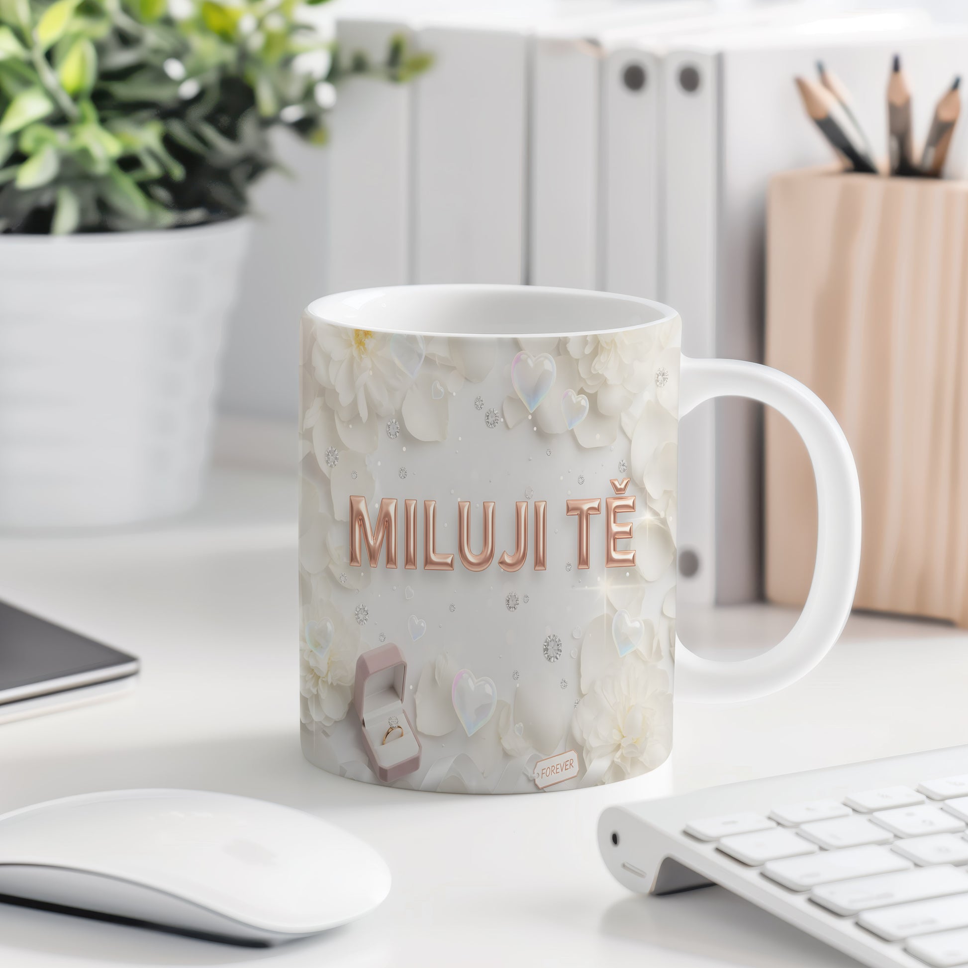 Bílý hrnek s nápisem MILUJI TĚ a květinovým motivem.