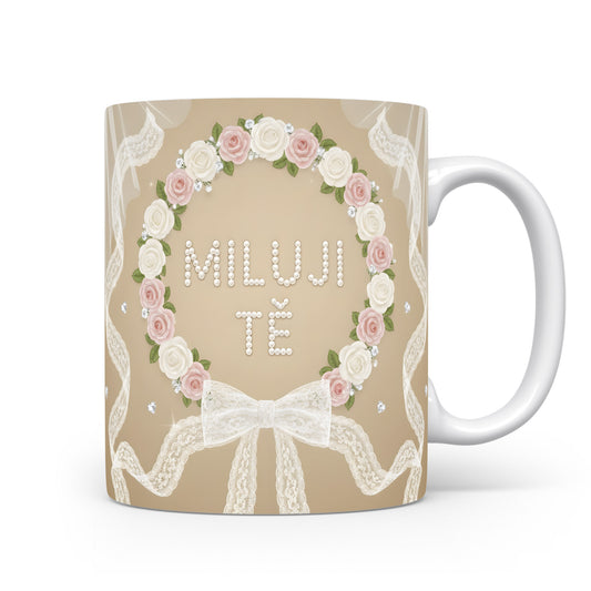 Hrnek s nápisem MILUJI TĚ, ozdobený růžemi a krajkou.