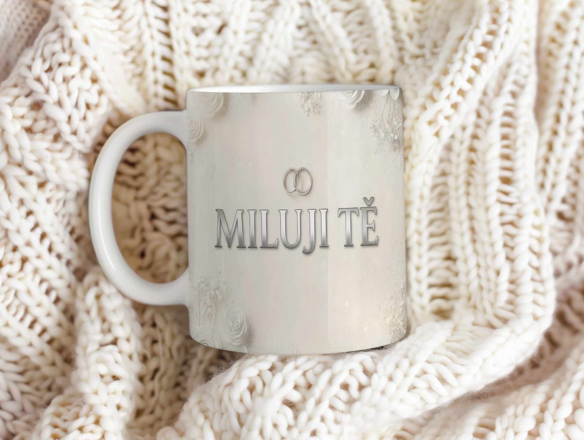 Bílý hrnek s nápisem MILUJI TĚ a květinovým motivem.