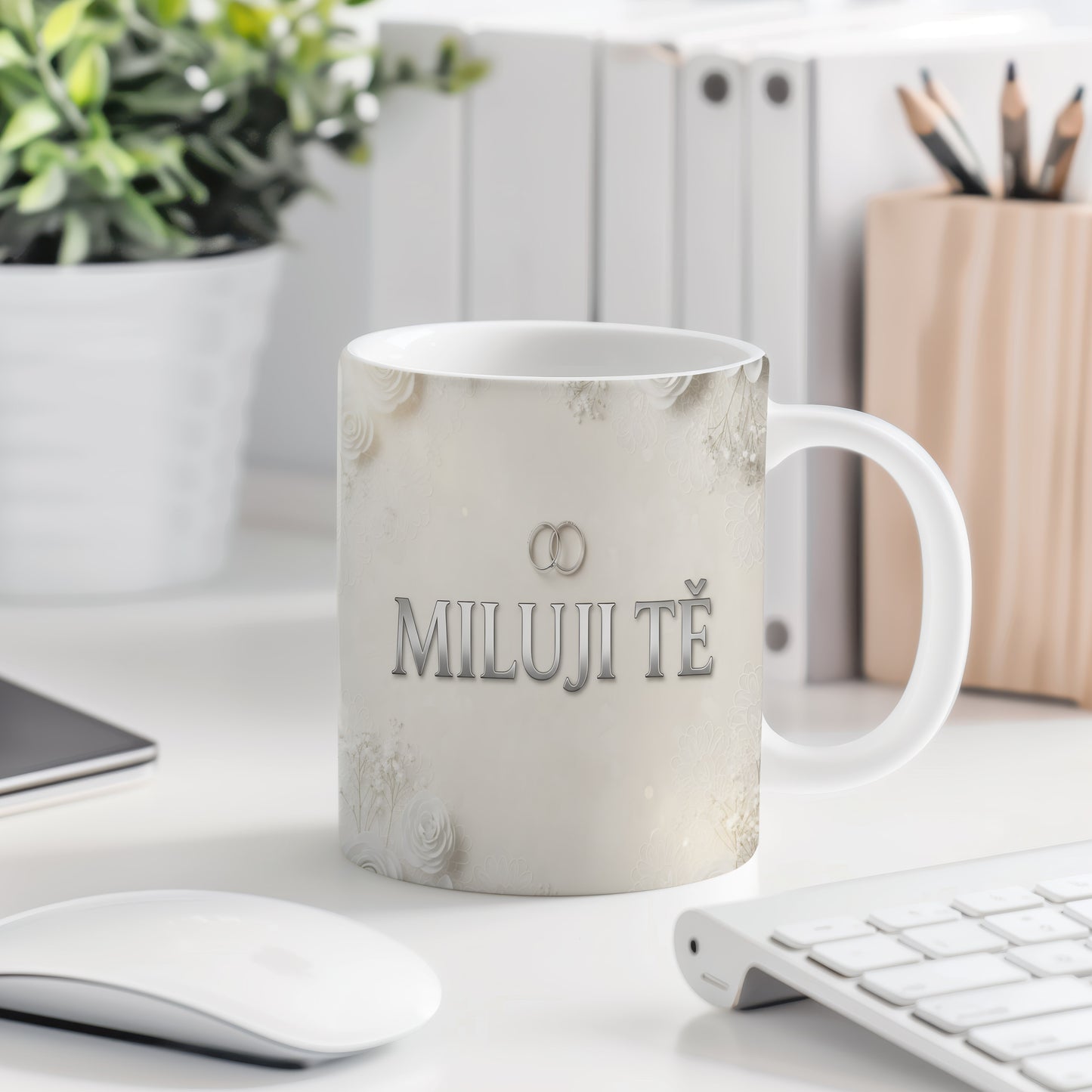 Bílý hrnek s nápisem MILUJI TĚ a květinovým motivem.