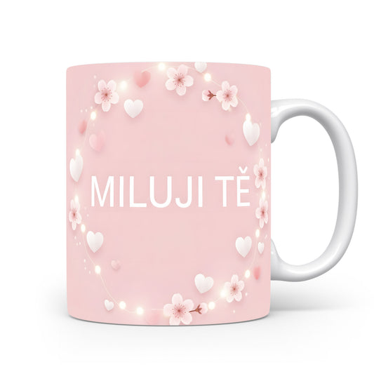 Světle růžový hrnek s nápisem MILUJI TĚ, ozdobený srdíčky a květinami.